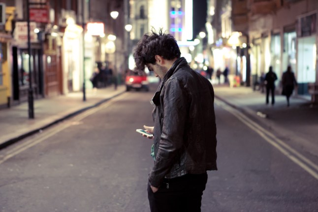 Young man checks phone as he crosses the road