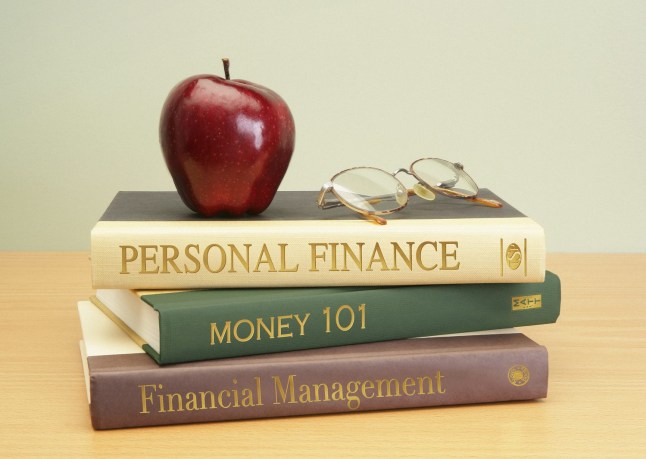 Stack of finance books on desk with apple and glasses