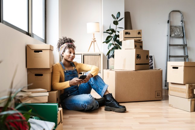 Thoughtful woman holding a mobile sitting on the floor of her new house while moving.